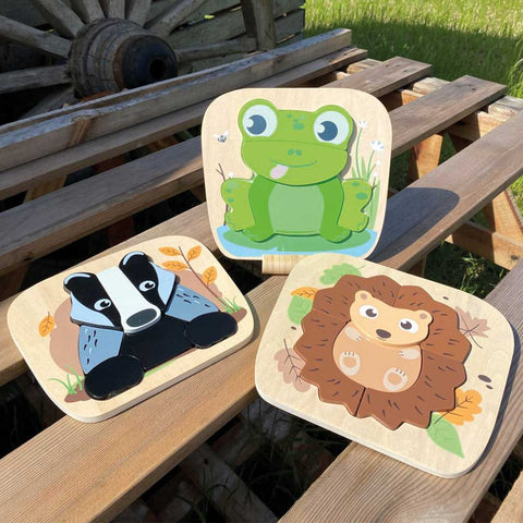 Brightly coloured wooden puzzles of frog, badger and hedgehog, displayed on a pallet table outside.